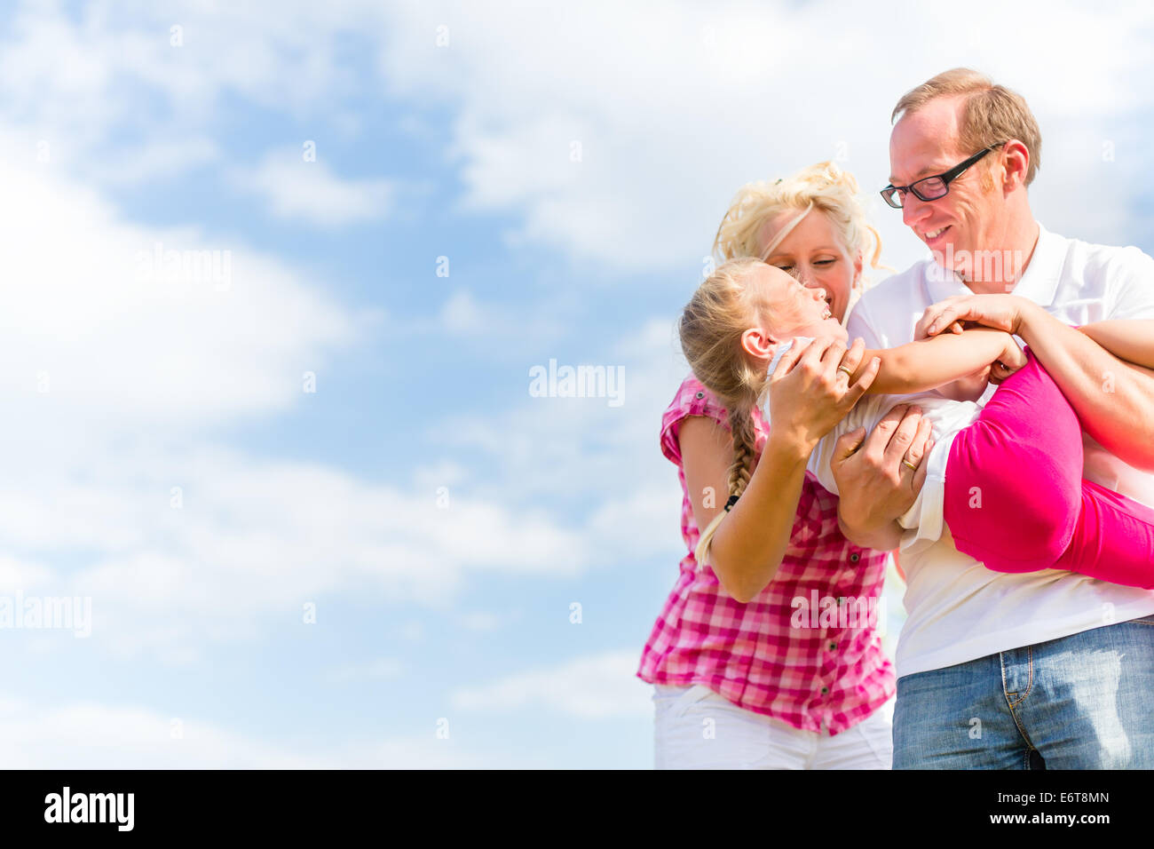Family romping on field with parents carrying child Stock Photo