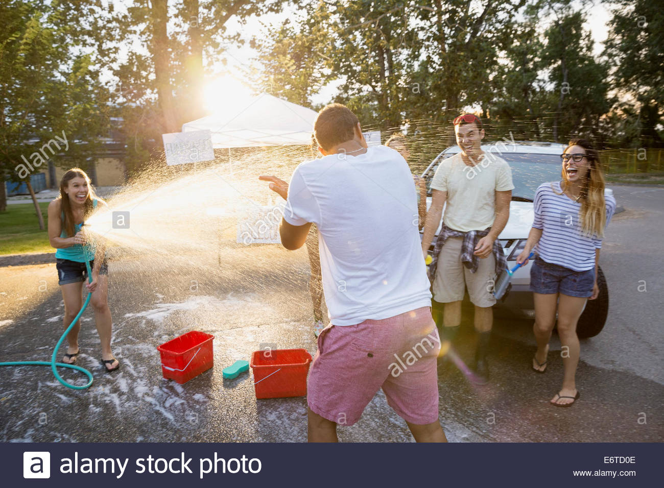 Woman spraying man with hose at car wash Stock Photo