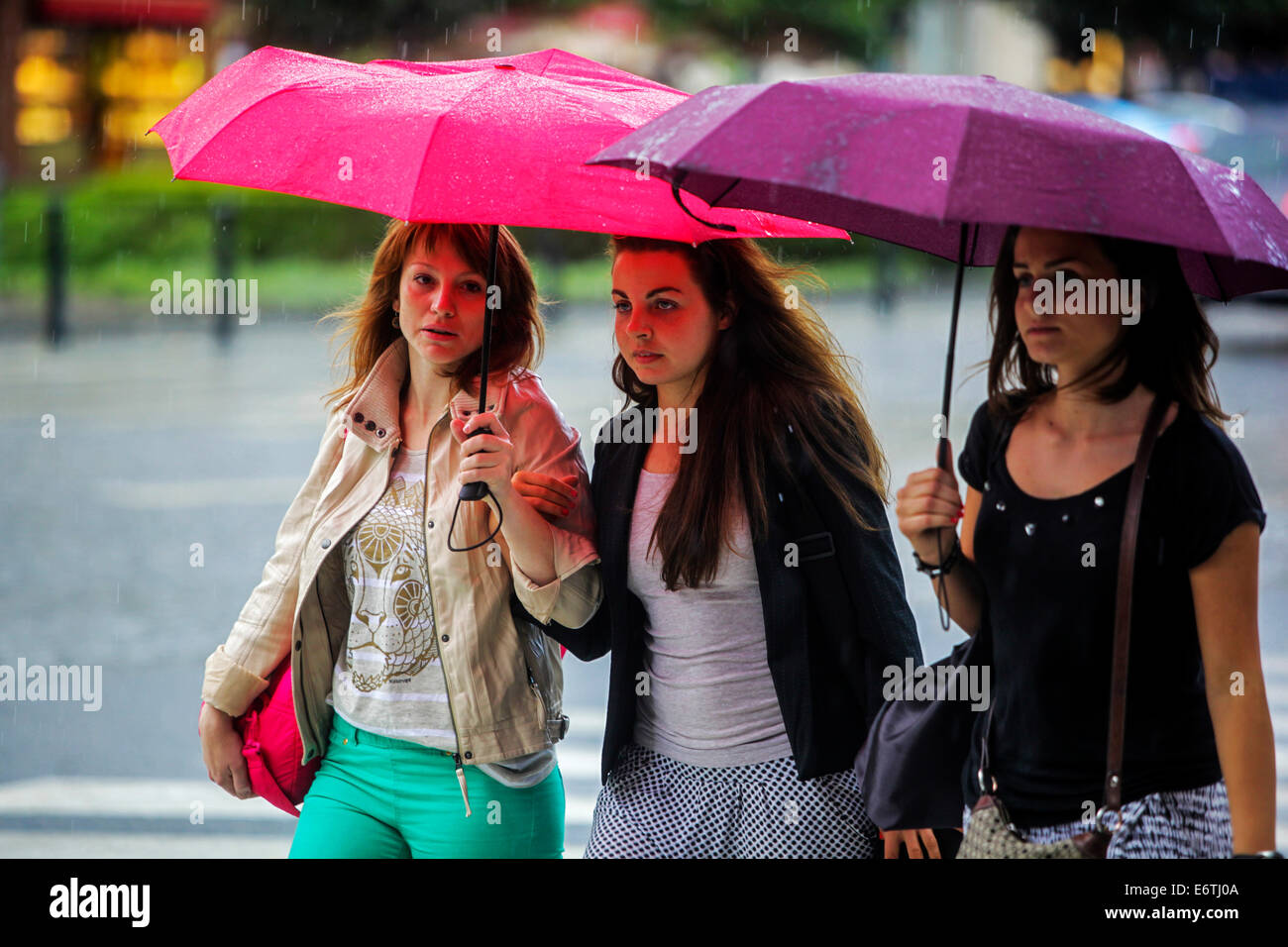 Three girls, young women under umbrellas in summer rain, city street people Rainy Weather Summer Forecast Stock Photo