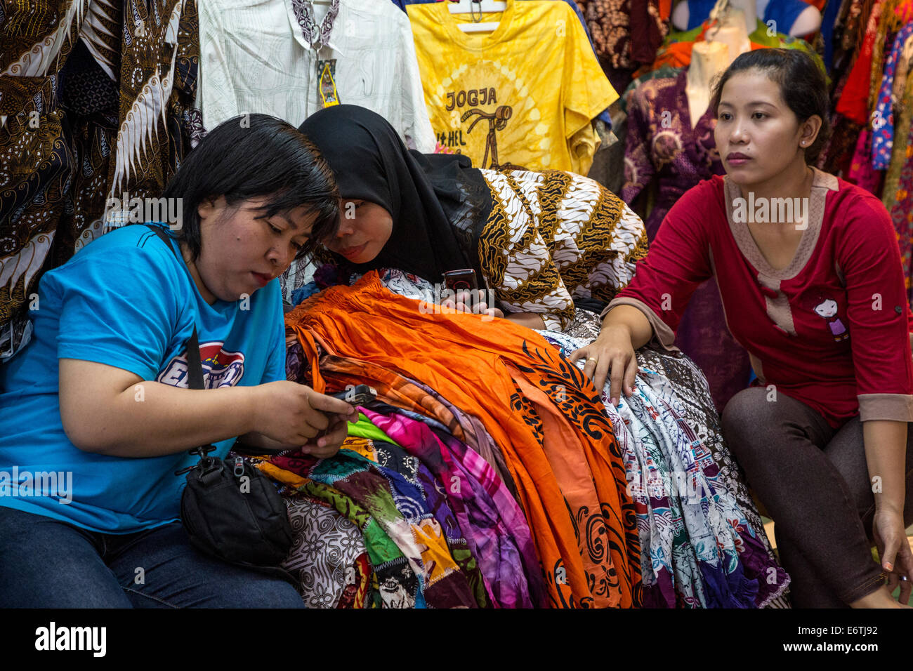 Yogyakarta, Java, Indonesia.  Young Women Checking Cell Phone in a Clothing Shop, Beringharjo Market. Stock Photo