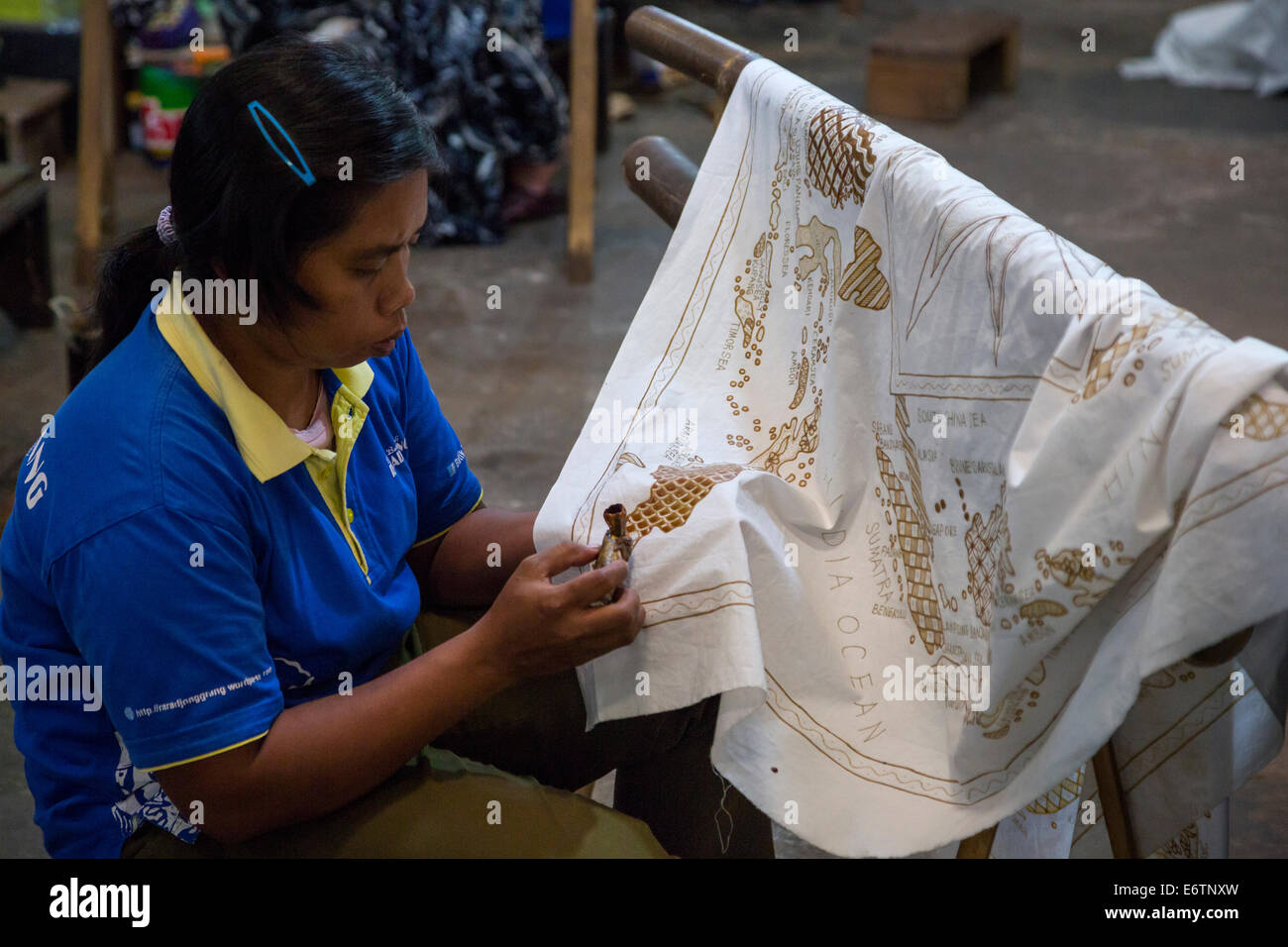Yogyakarta, Java, Indonesia.  Batik Design Artist Applying Wax to Design Sketch on Cloth, a map of the Indonesian islands. Stock Photo