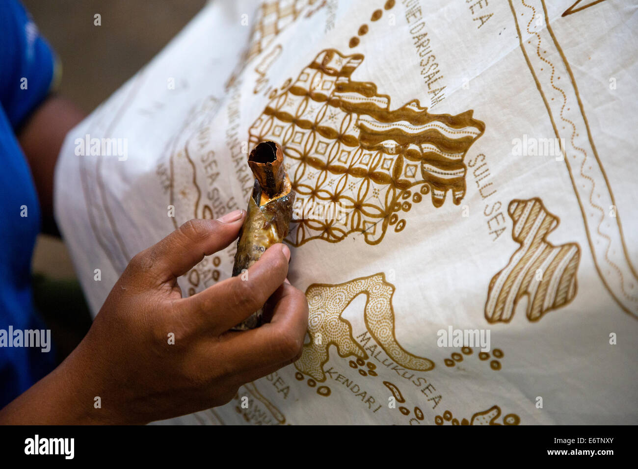 Yogyakarta, Java, Indonesia.  Batik Design Artist Applying Wax to Design Sketch on Cloth, a map of the Indonesian islands. Stock Photo
