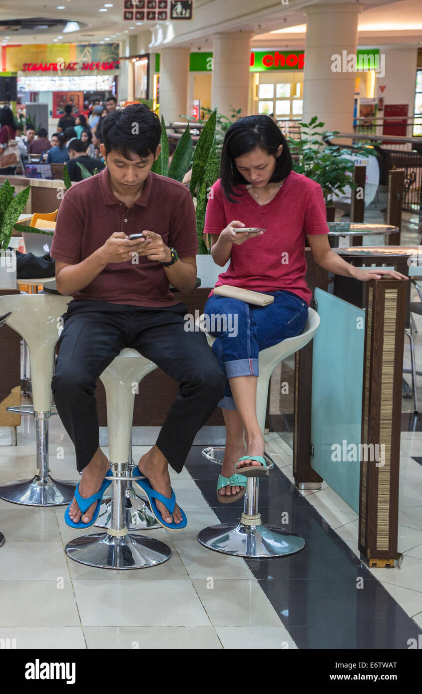 Yogyakarta, Java, Indonesia.  Ambarrukmo Shopping Mall.  Young Javanese Couple Checking Cell Phones in the Food Court. Stock Photo