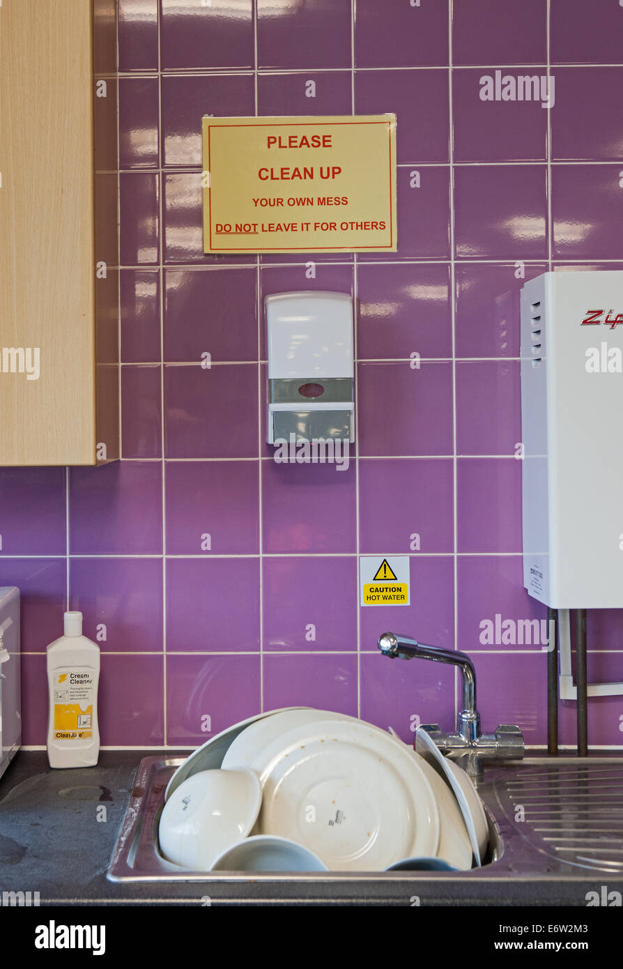 A pile of plates and dishes under a 'please clean up your own mess sign' Stock Photo Alamy