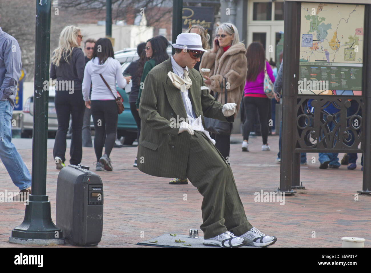Male living statue street busker performs for tips in a suit leaning at an impossible angle in downtown Asheville, NC Stock Photo
