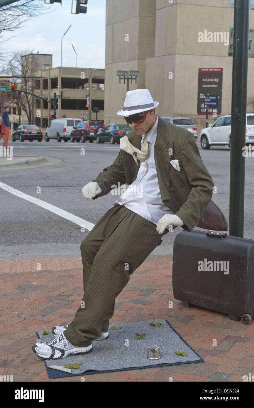 Asheville, North Carolina, USA - March 2, 2014: Living statue street artist showing a man in a suit being blown backward Stock Photo