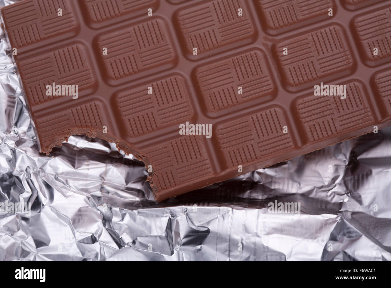 Bitten a piece of chocolate bar in silver foil packaging. Stock Photo