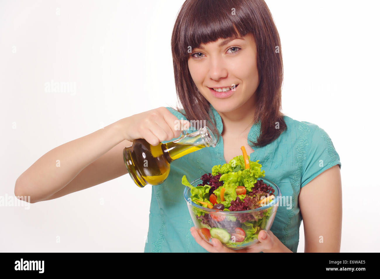 Young happy woman making salad with vegetables and oil. Stock Photo