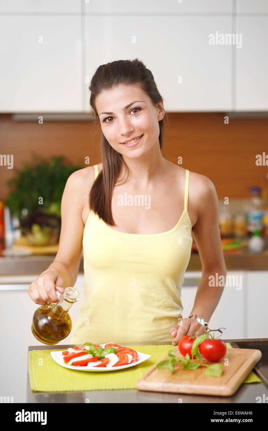 Young woman making salad with tomatoes, cheese, basil and oil  in the kitchen. Stock Photo
