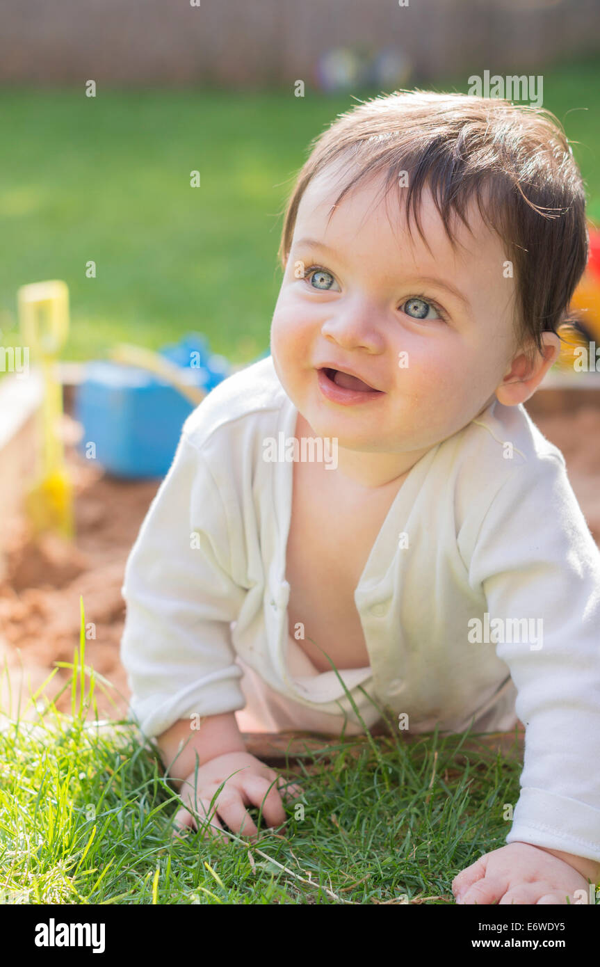 Baby climbing out of a sandpit during the summer. Stock Photo
