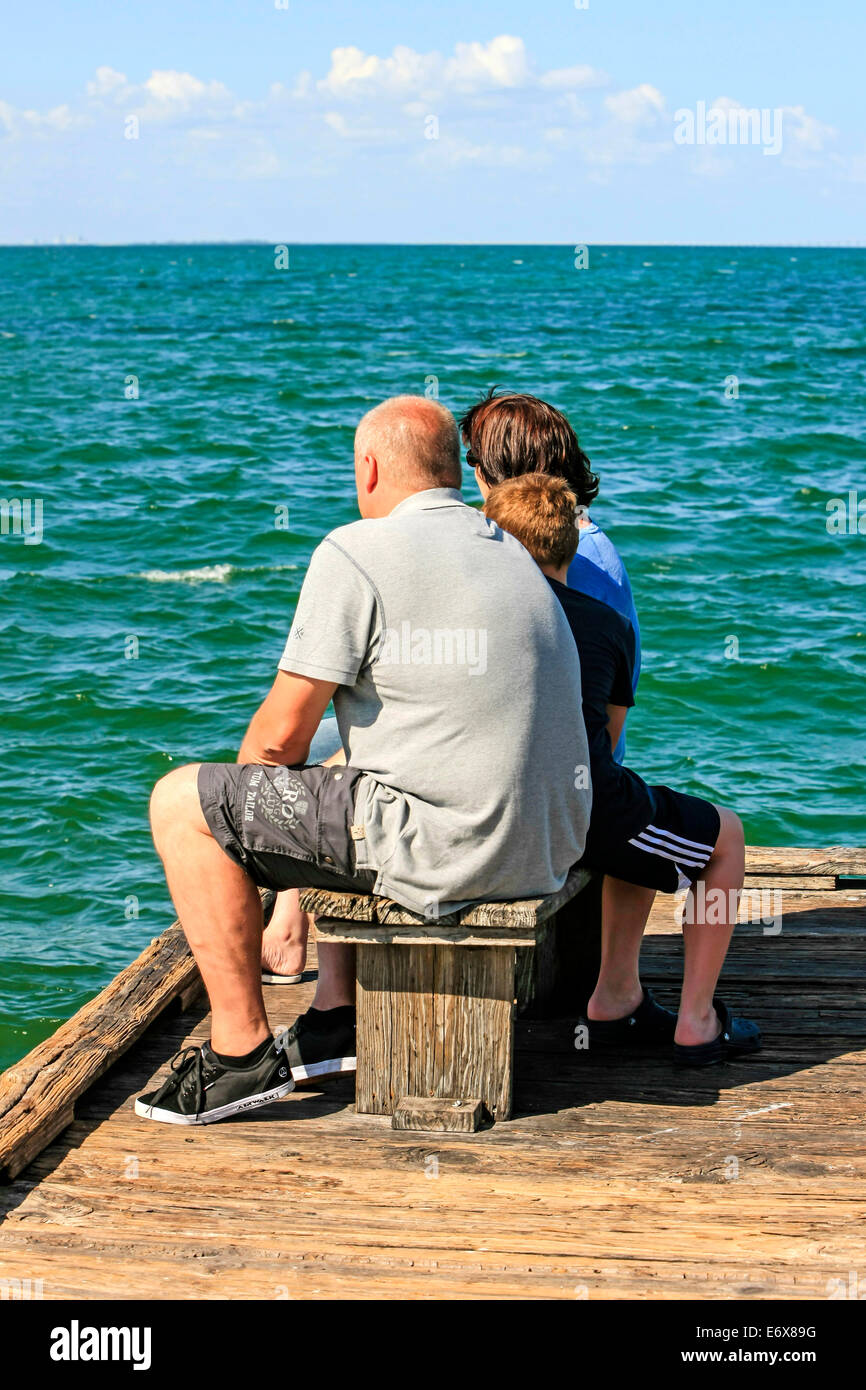 A tight family group sit on a bench seat watching the waters from Anna Maria Pier in Bradenton FL Stock Photo