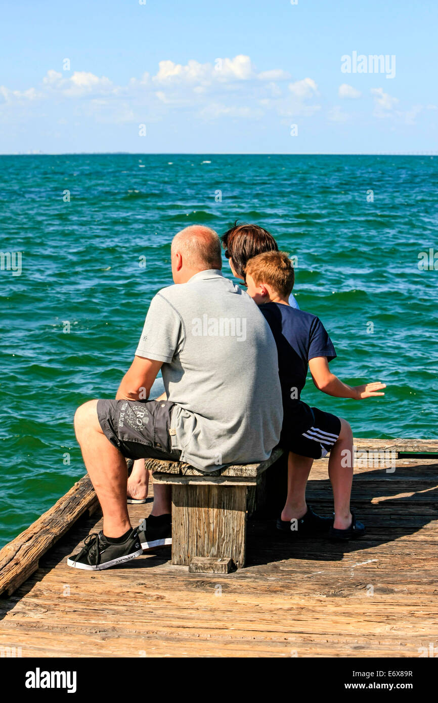 A tight family group sit on a bench seat watching the waters from Anna Maria Pier in Bradenton FL Stock Photo