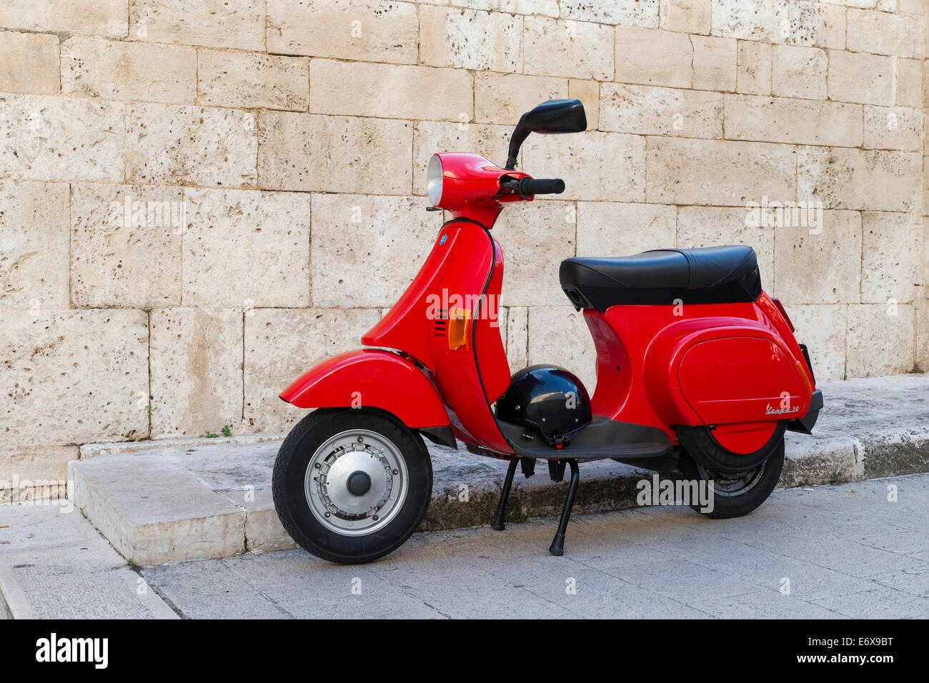 Vespa 50, red scooter with helmet parked in front of a wall, Alberobello, Apulia, Italy Stock Photo