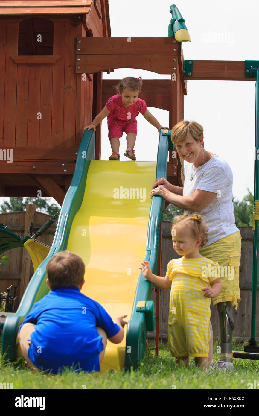 Grandmother with a prosthetic leg playing on a slide with her grandchildren Stock Photo