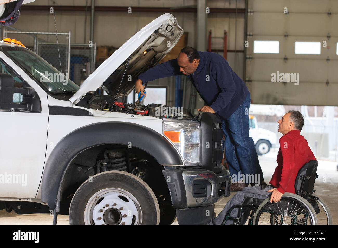 Technician performing engine maintenance with supervisor in wheelchair Stock Photo Alamy