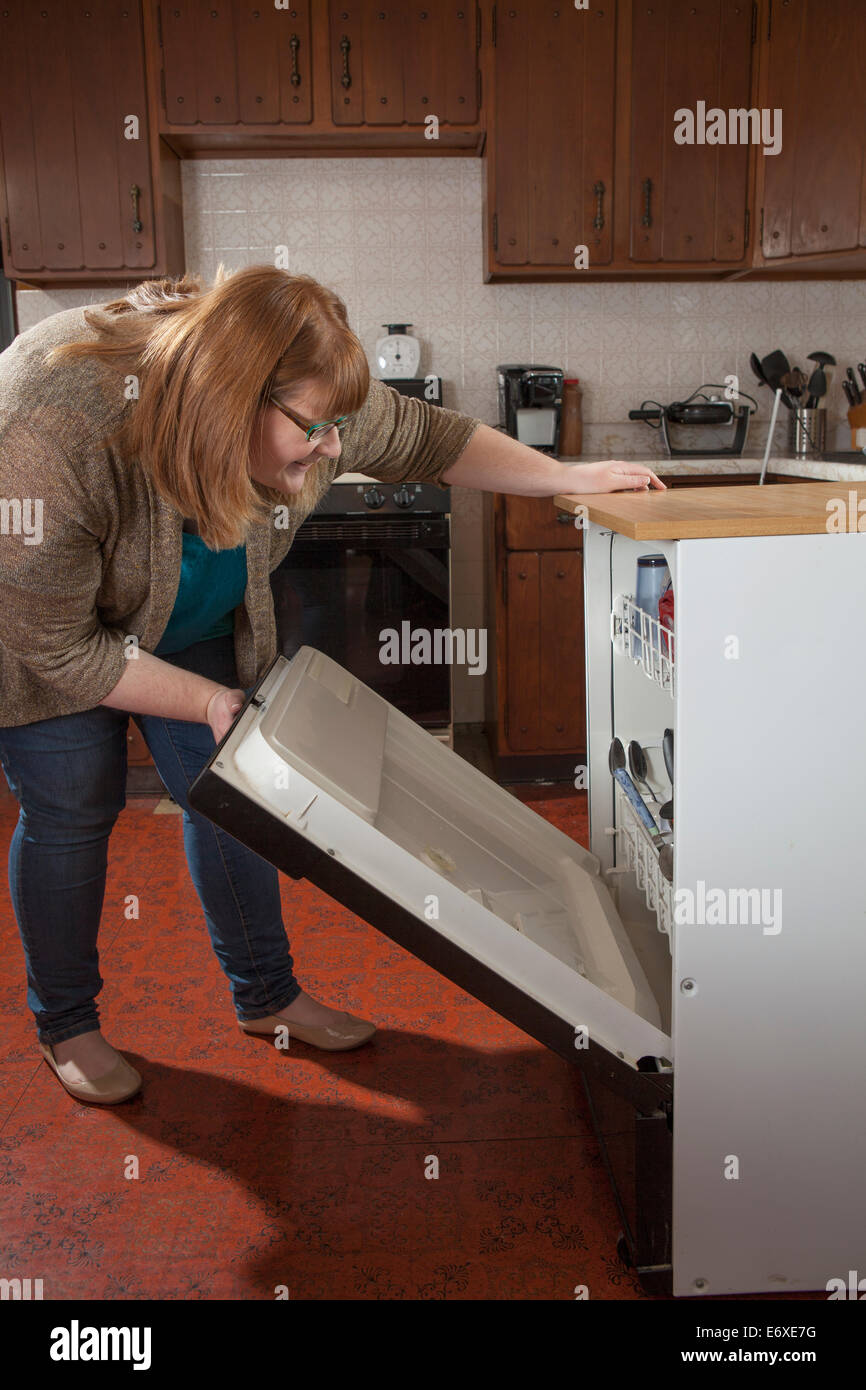 Woman who is legally blind loading the dishwasher in her kitchen Stock