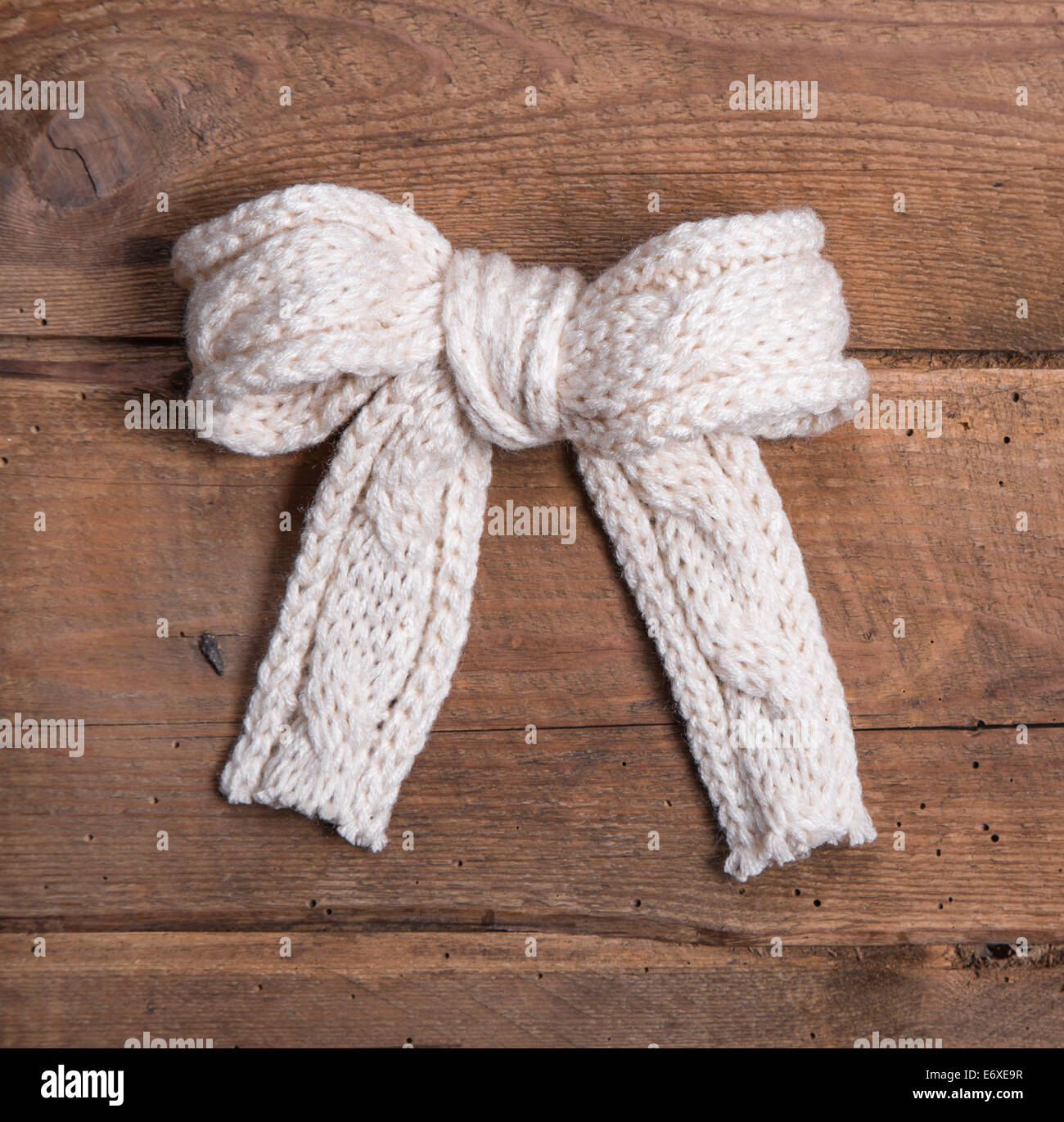 White knitted woolen bow on square wooden background - voucher or coupon for christmas Stock Photo