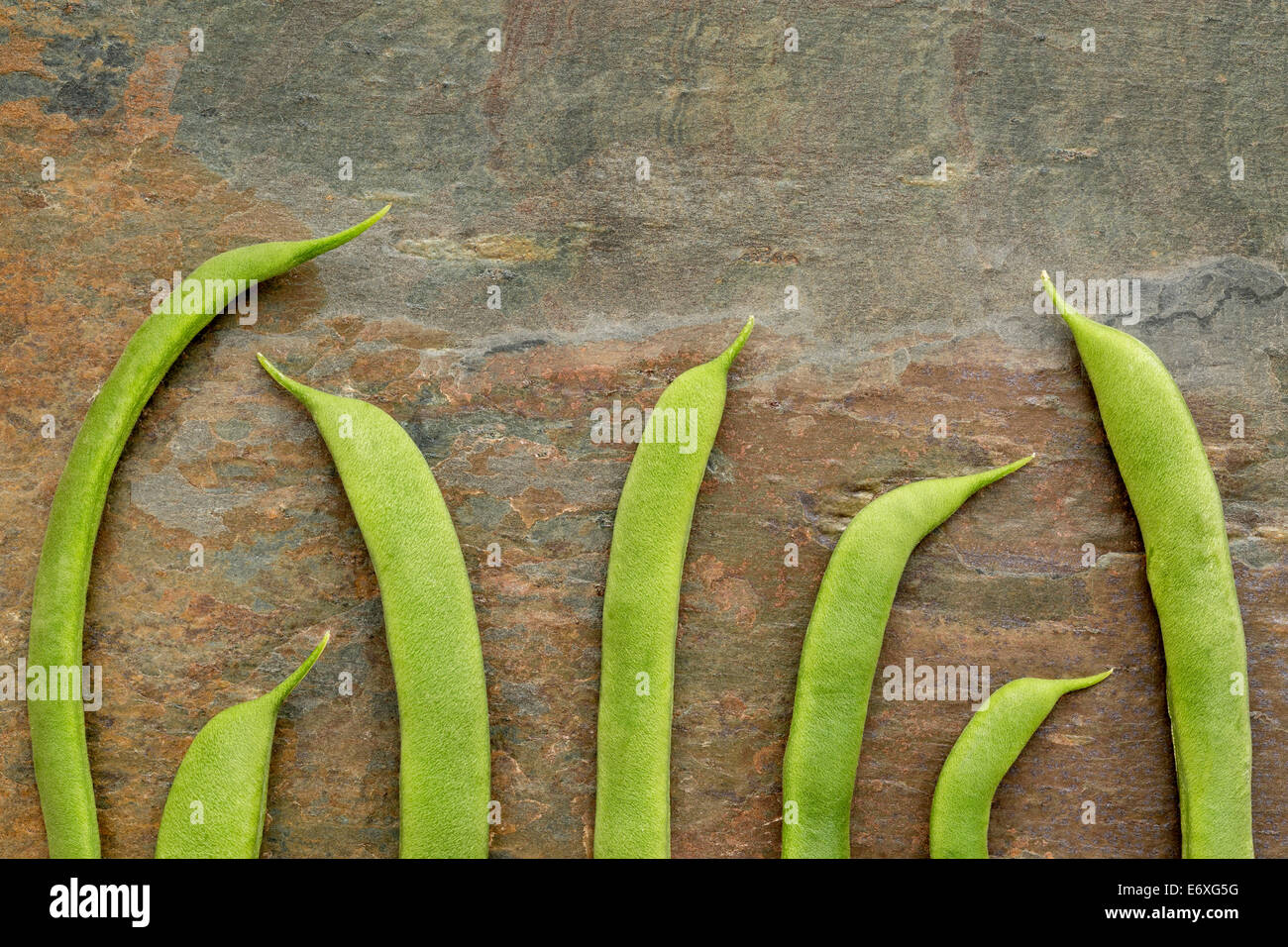 pods of fresh green French beans against slate rock background Stock Photo