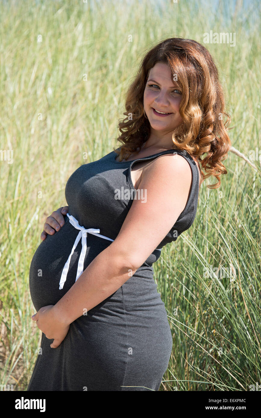 pregnant woman with white ribbon bow on her belly in nature with straw background Stock Photo