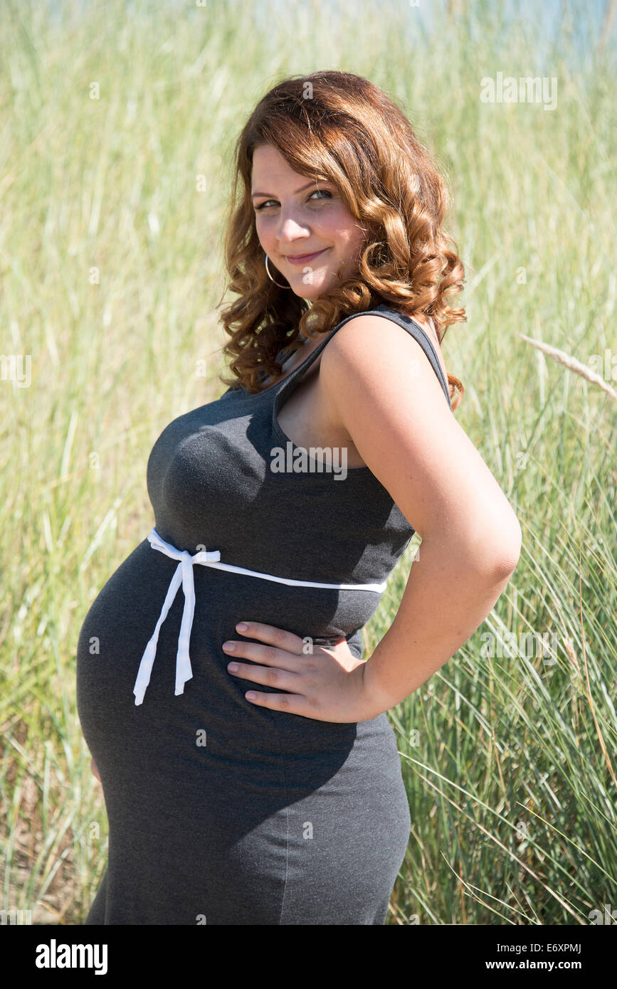 pregnant woman with white ribbon bow on her belly in nature with straw background Stock Photo