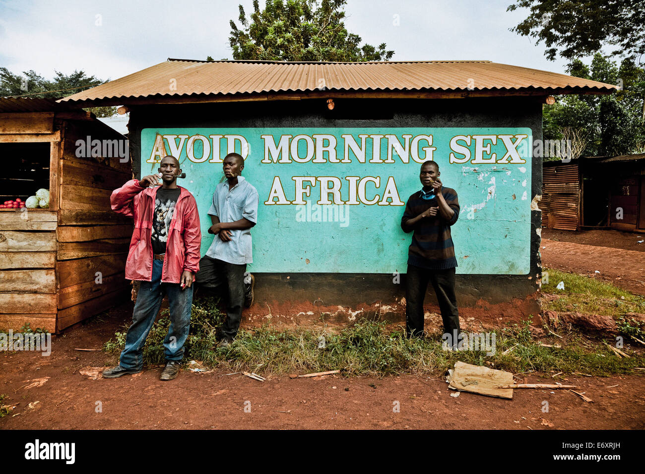 Three men smoking pipes in front of a hut with Anti-Aids campaign, Buwenda, Uganda, Africa Stock Photo