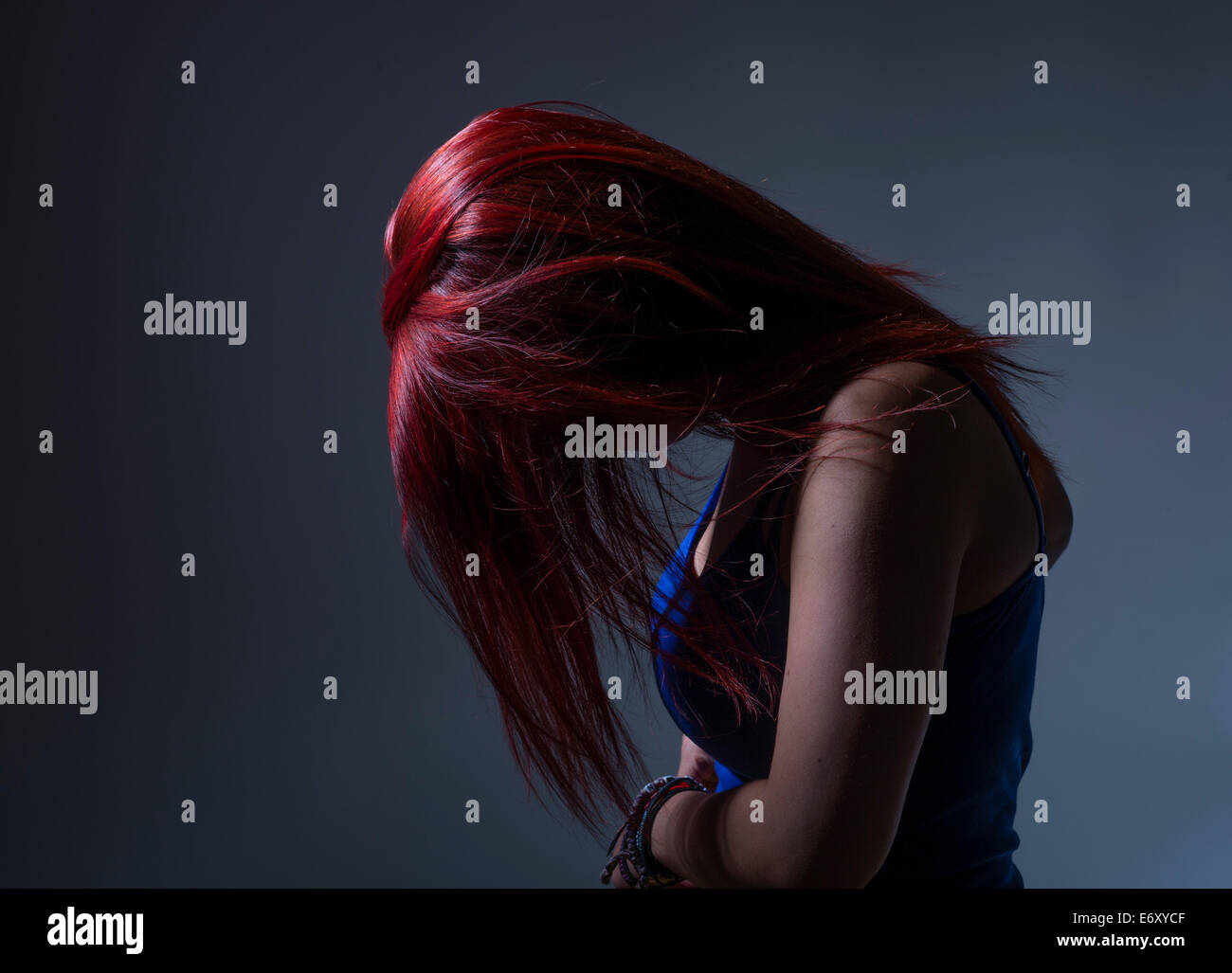 Sadness / Depression:  A young woman teenage girl in profile with dyed bright red hair, head bowed obscuring her face, UK Stock Photo