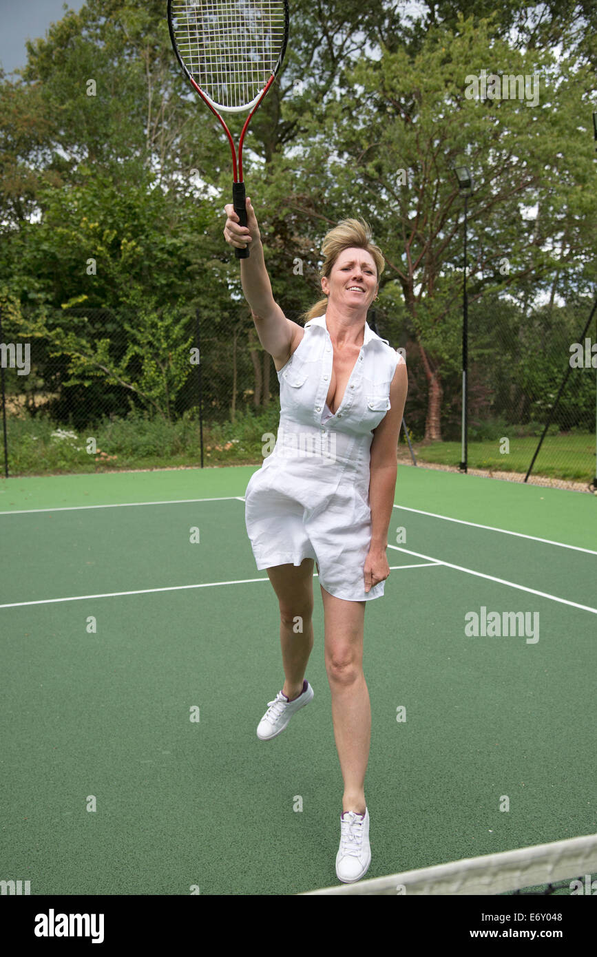 Female tennis player in action on a court stretching to hit the ball Stock Photo