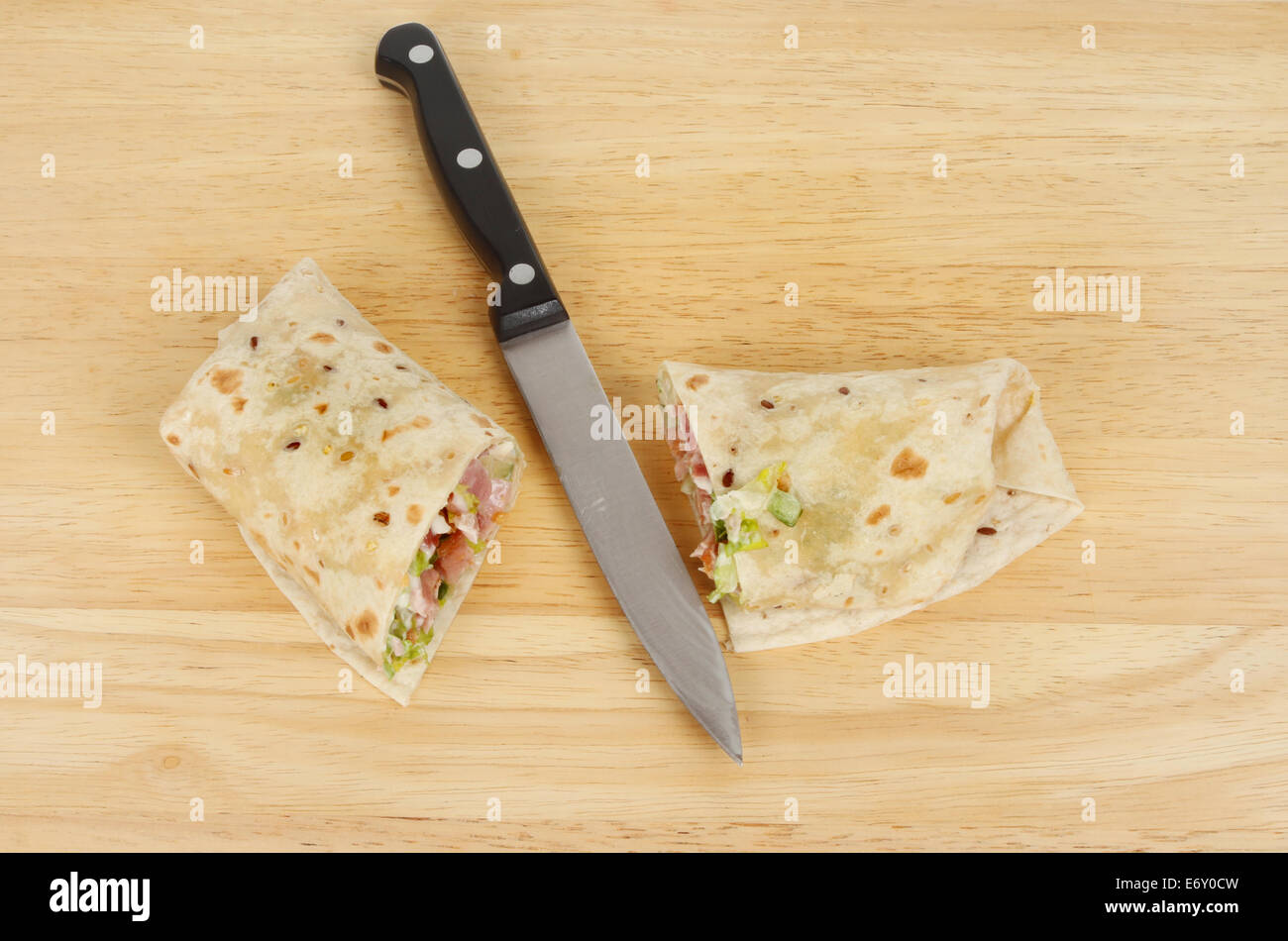 Cut bacon and salad bread wrap with a knife on a wooden board Stock Photo