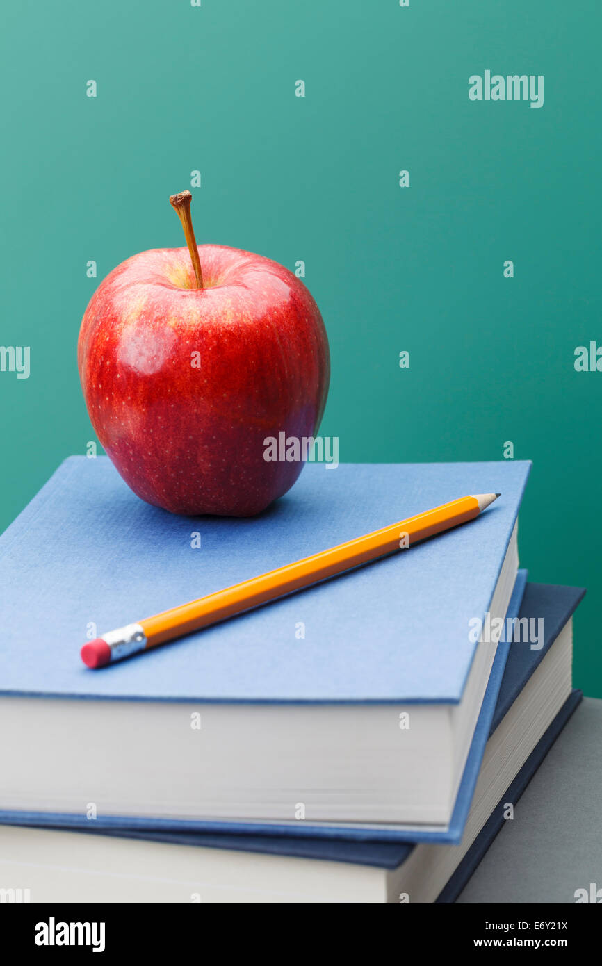 Green Chalkboard, School Books, Sharpened Yellow Pencil and Red Apple in Classroom Setting with Copy Space. Stock Photo