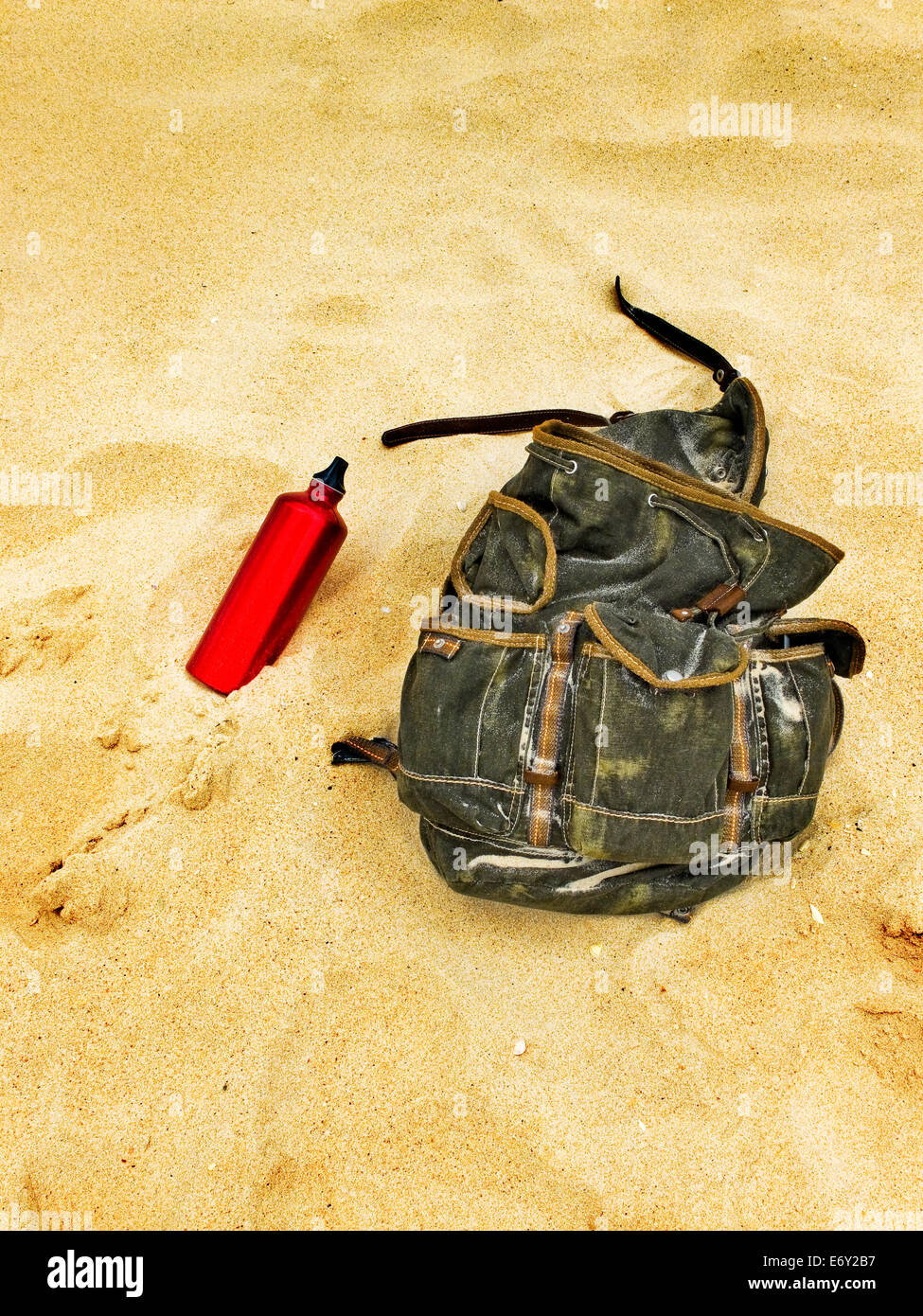 Backpack and canteen water bottle in the sand of a beach. Backpacking traveller taking a break. Stock Photo
