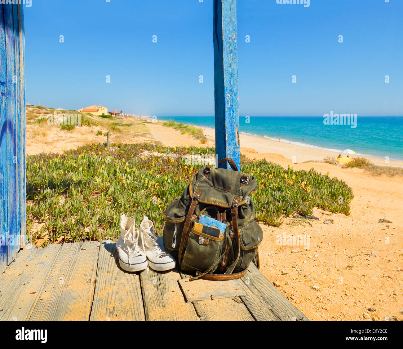 Backpack and shoes on the porch of a wooden hut next to the shore of a European beach. Backpacking traveller taking a break in a Stock Photo