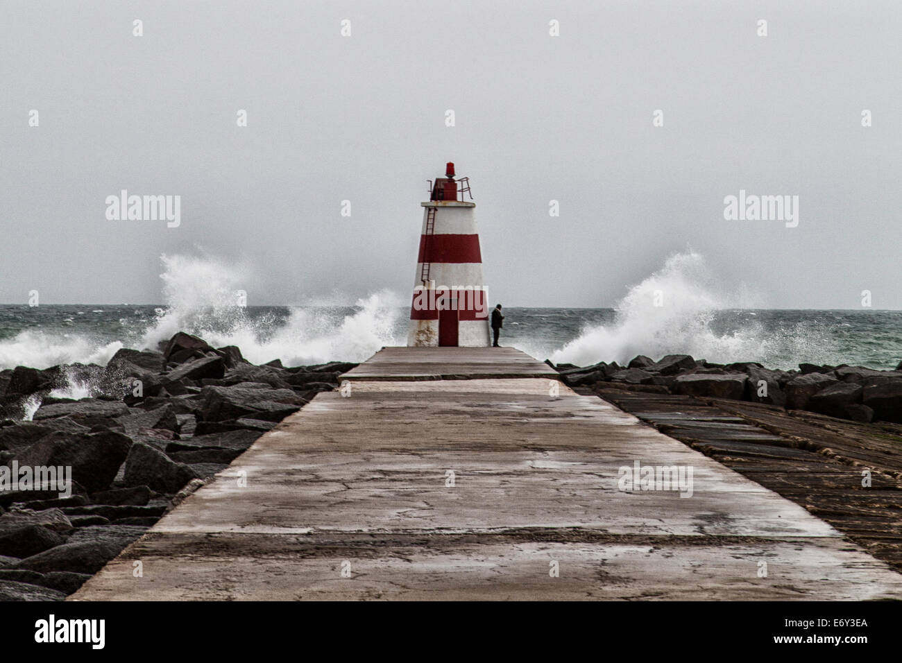 Standing at the end of the pier, waves crashing around the lighthouse. A long walk back. Stock Photo