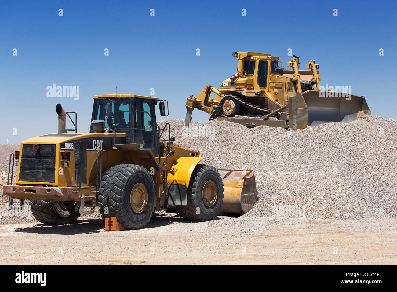 A CAT 980G Front End Loader is parked below a CAT D9 Dozer that is parked on a pile of aggregate Stock Photo