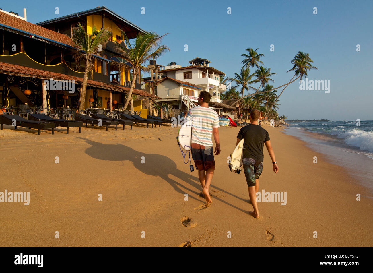 Two male surfers carrying their boards on the beach at Hikkaduwa, Sri Lanka West Coast. South Asia Stock Photo