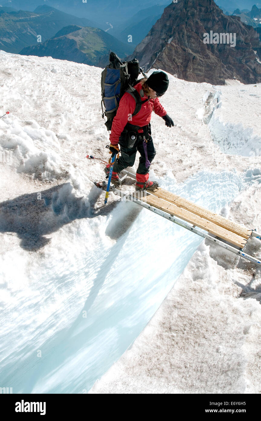 Mountain climber Mike Huckaby crosses a ladder which spans a crevasse on Mt Rainer's Disappointment Cleaver route, Washington St Stock Photo