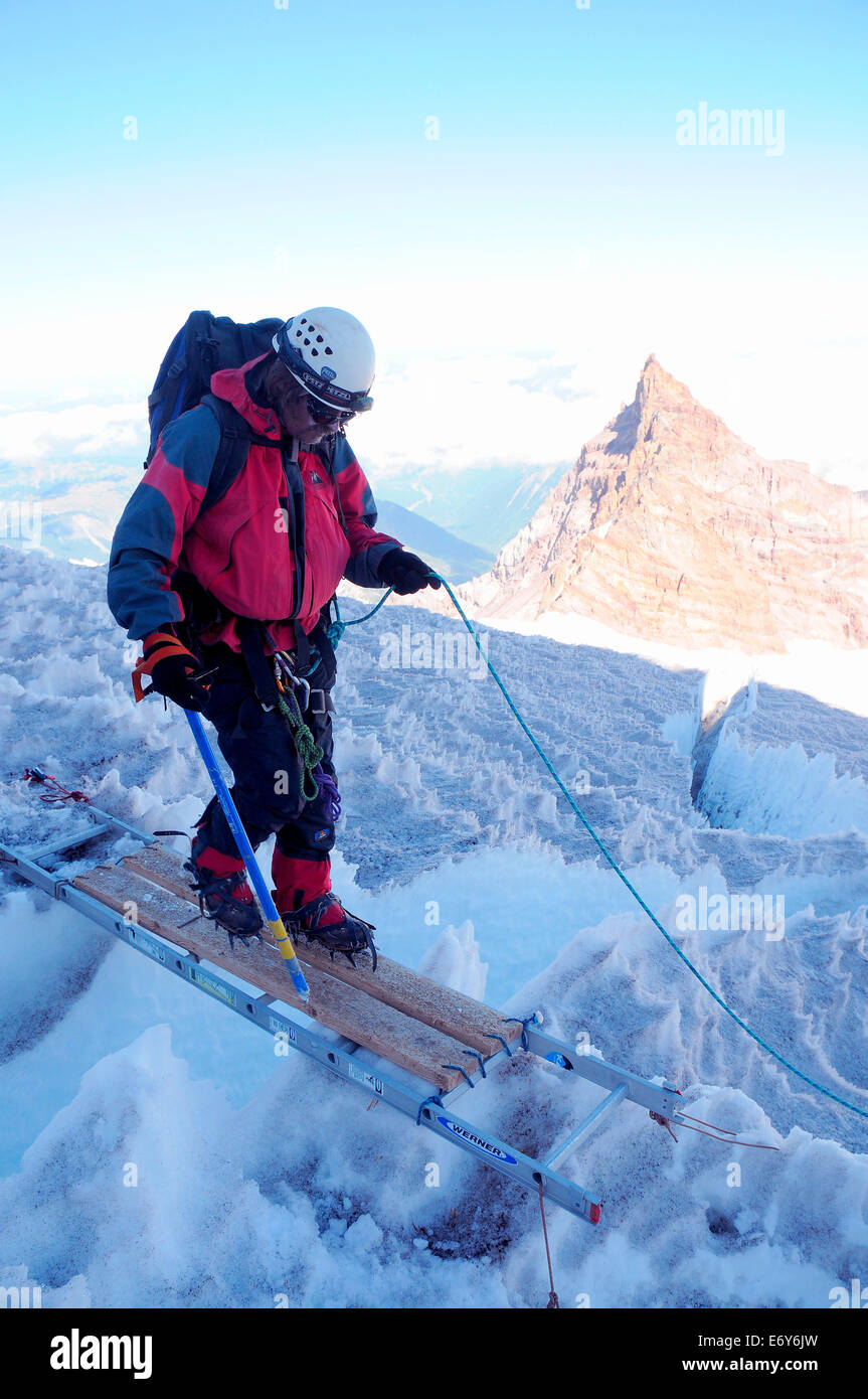 Mike Huckaby crosses a ladder which spans a crevasse on the shoulder of Mt Rainer Stock Photo