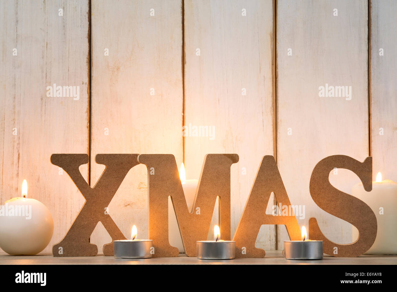 Wooden letters spelling Xmas and burning candles on wood plank Stock Photo