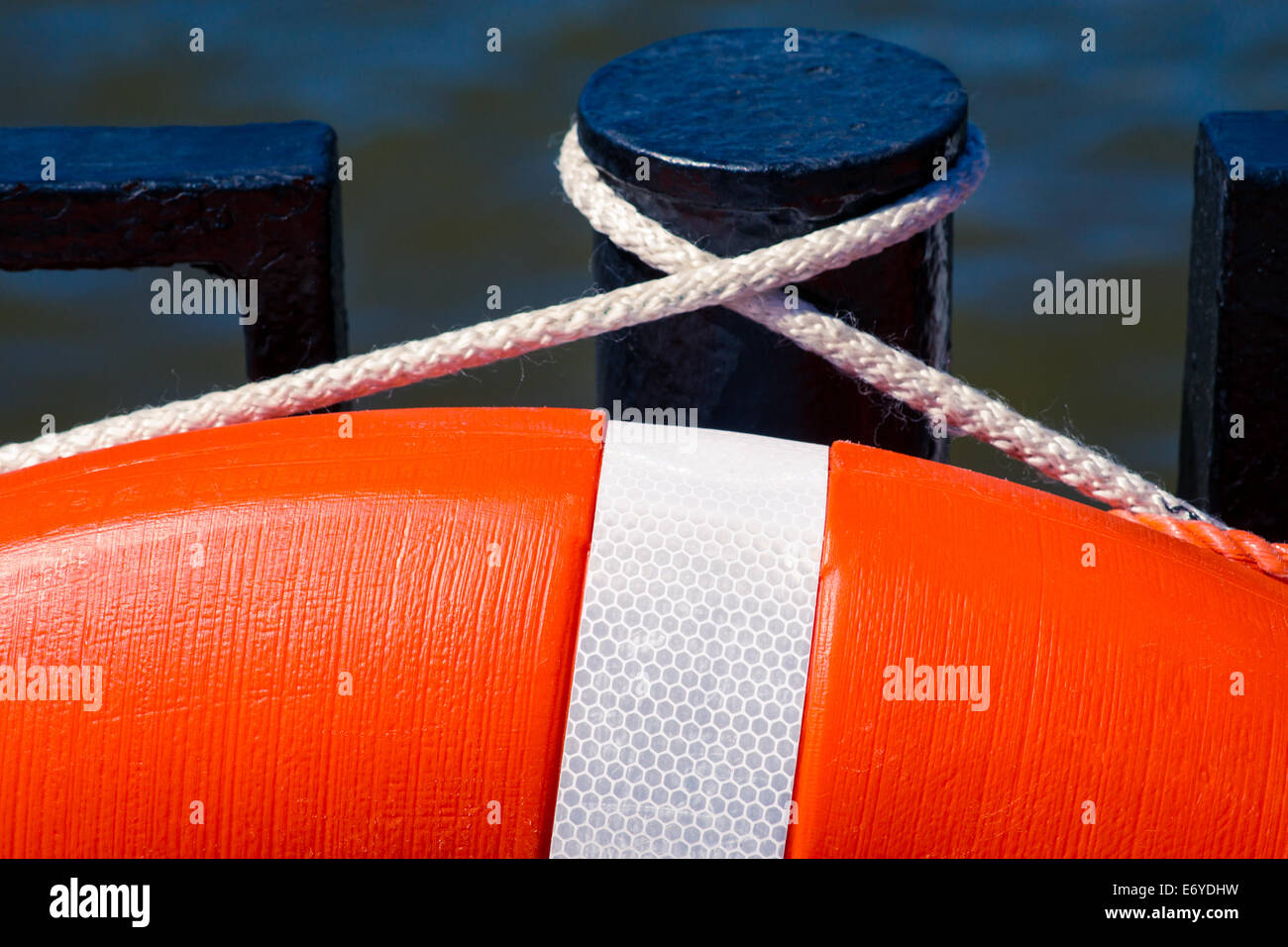 Detail of the orange live saving ring hanging on a black pole against dark water Stock Photo