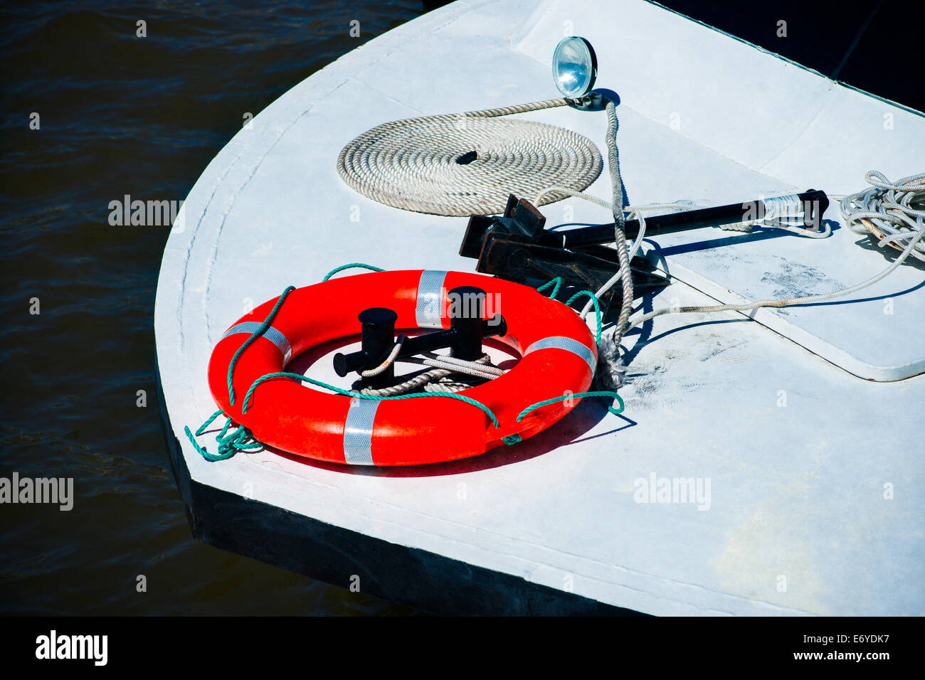 Bow of the small leisure boat. Red safety ring on the white deck. Black anchor and bight of rope Stock Photo