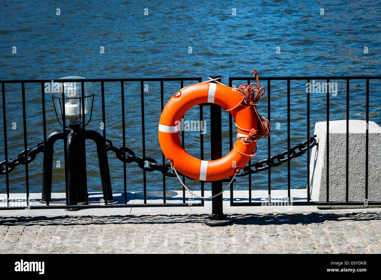 Orange life saving ring on a black pole of the protective fence of the embankment Stock Photo