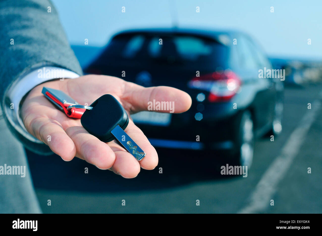 man in suit offering a car key to the observer, with a car in the background Stock Photo