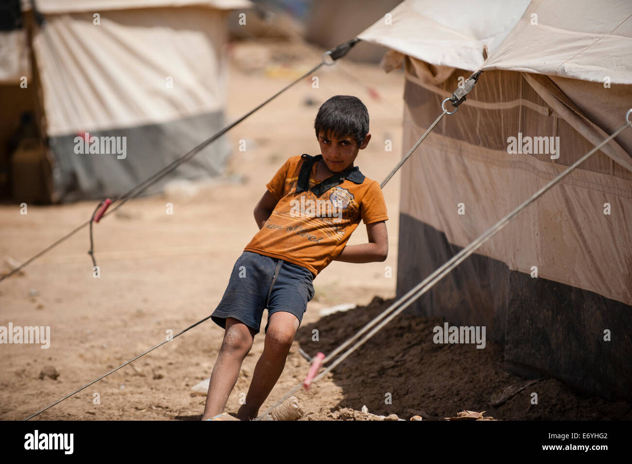A young boy rests on the guy ropes of a tent in Khazir Refugee Camp. It is a transit camp for people fled from the ISIS/ISIL threat in Mosul, Iraq/Kurdistan. The camp started on June 10, 2014, and sheltered 700 people who are mostly Muslim. © Martin Alan Smith/Pacific Press/Alamy Live News Stock Photo