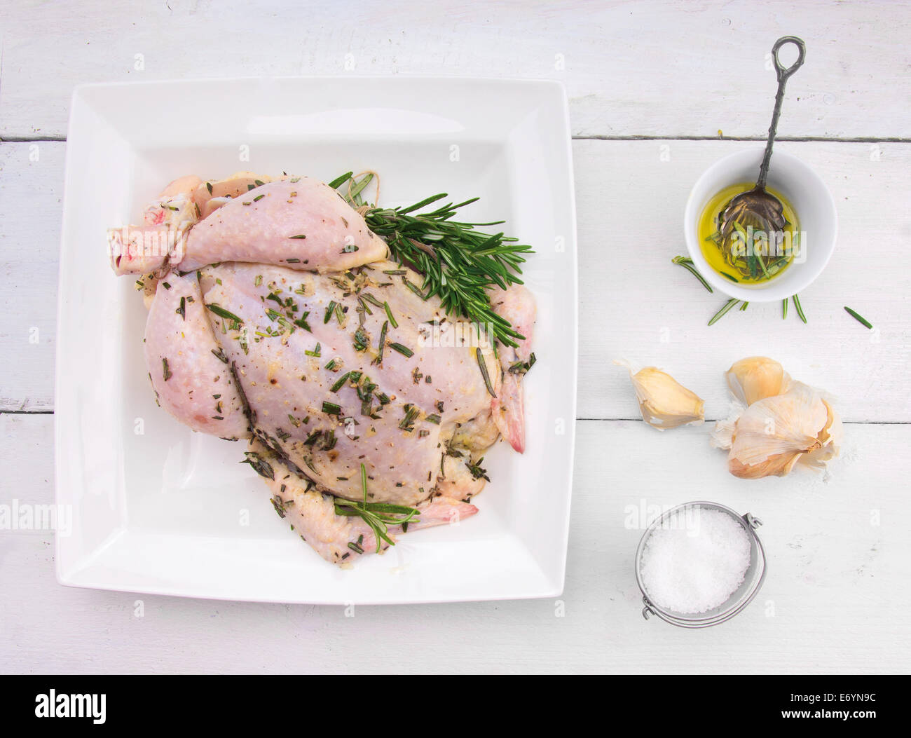 whole chicken with oil, rosemary, garlic and salt, preparation for grill roasting on white