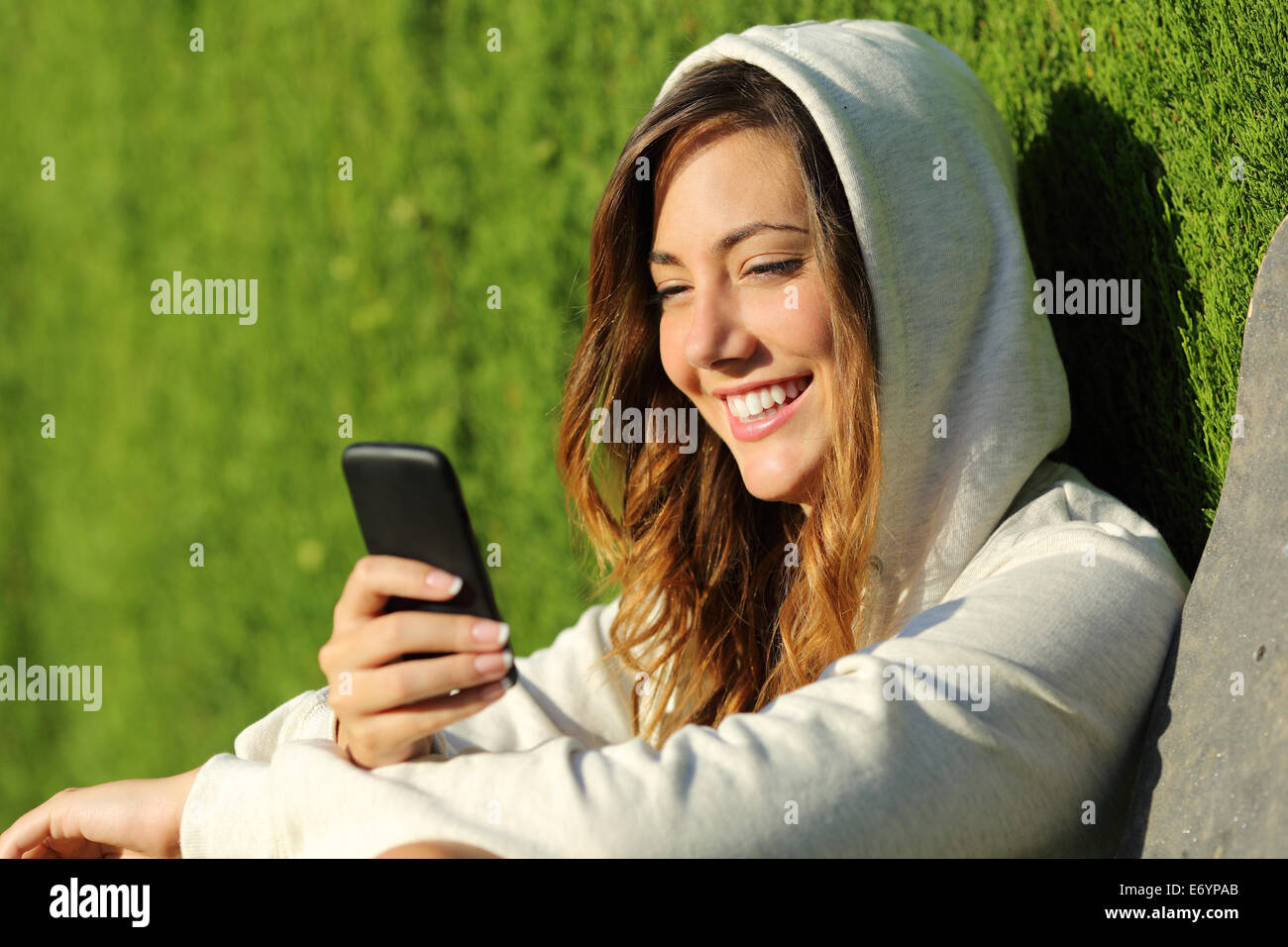 Modern teenager girl using a smart phone in a park with a green background Stock Photo