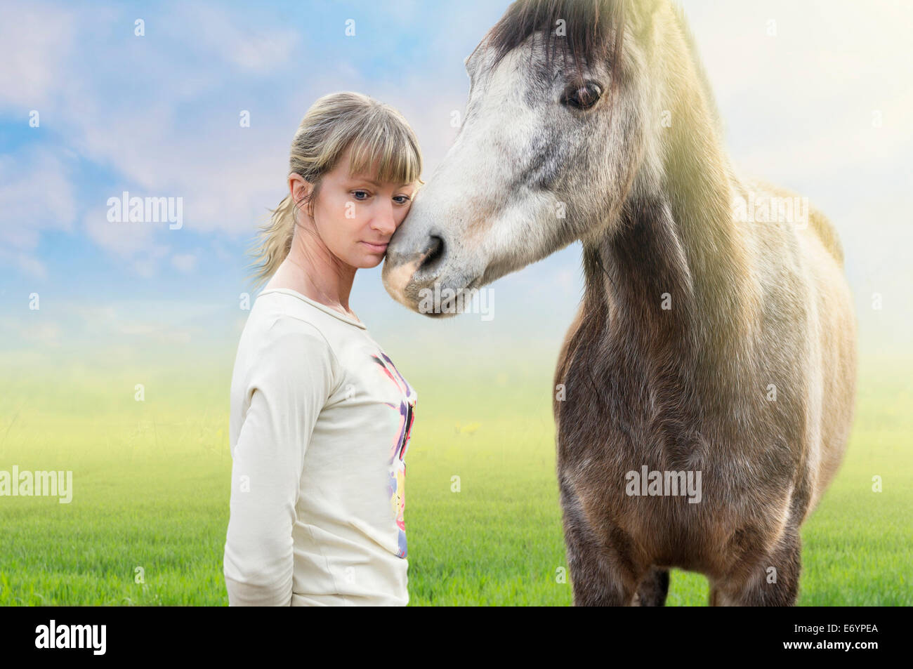 Horse cuddle with woman, summer background with green grass Stock Photo