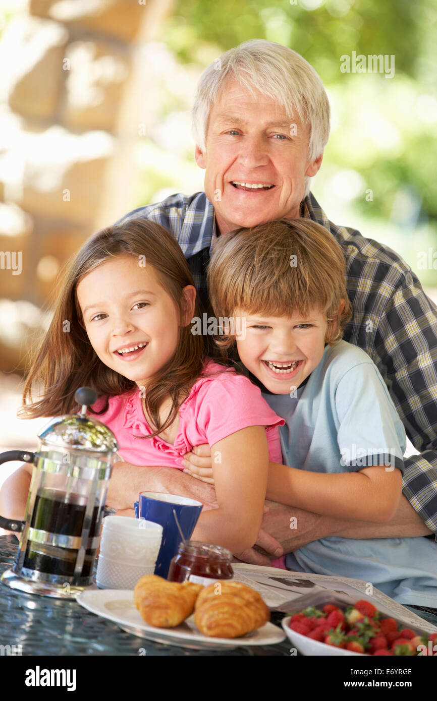 Mid age man and grandchildren eating breakfast outdoors Stock Photo