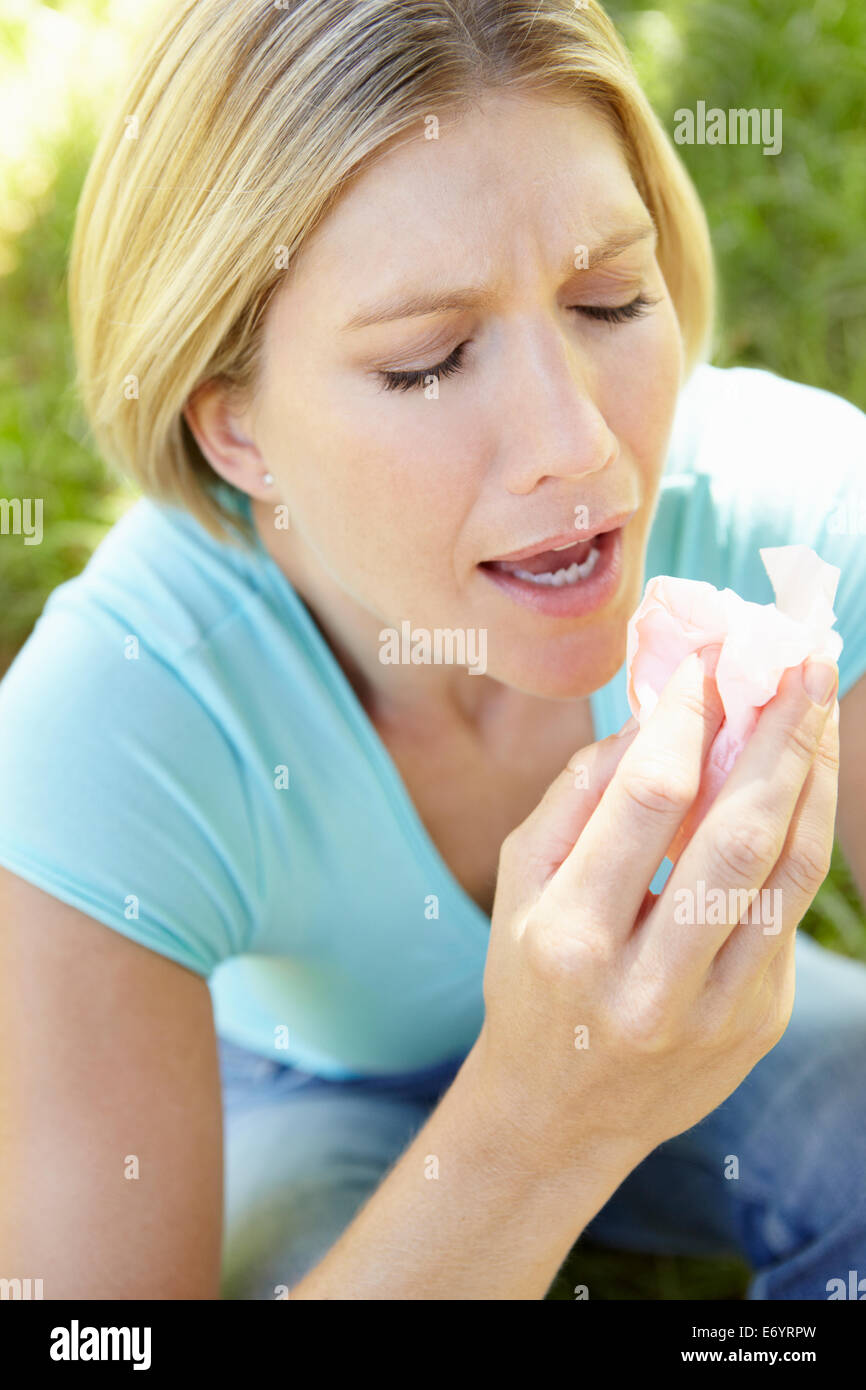 Woman sitting on grass sneezing Stock Photo