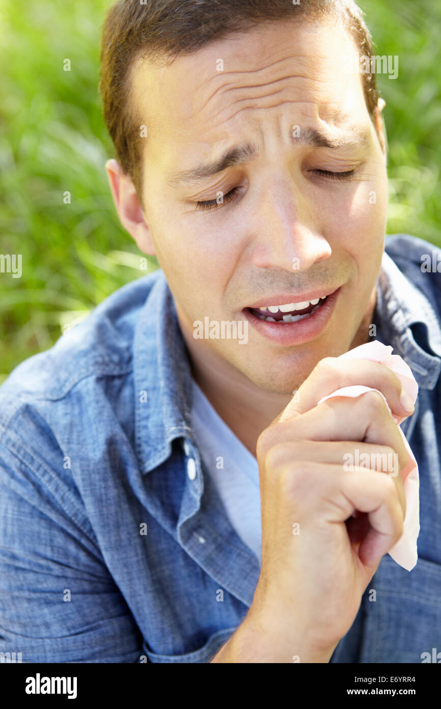 Man sitting on grass sneezing Stock Photo