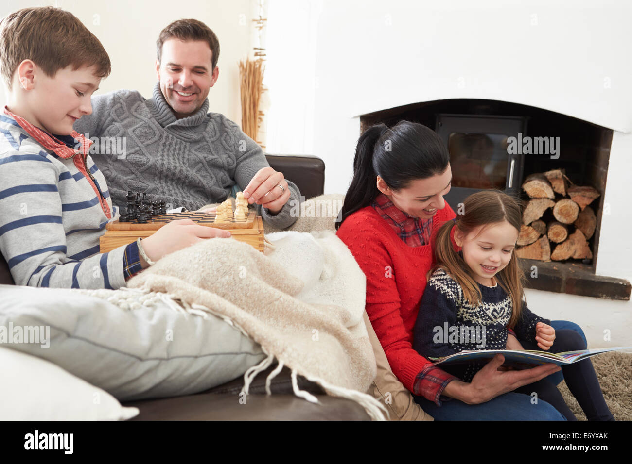 Family Relaxing Indoors Playing Chess And Reading Book Stock Photo