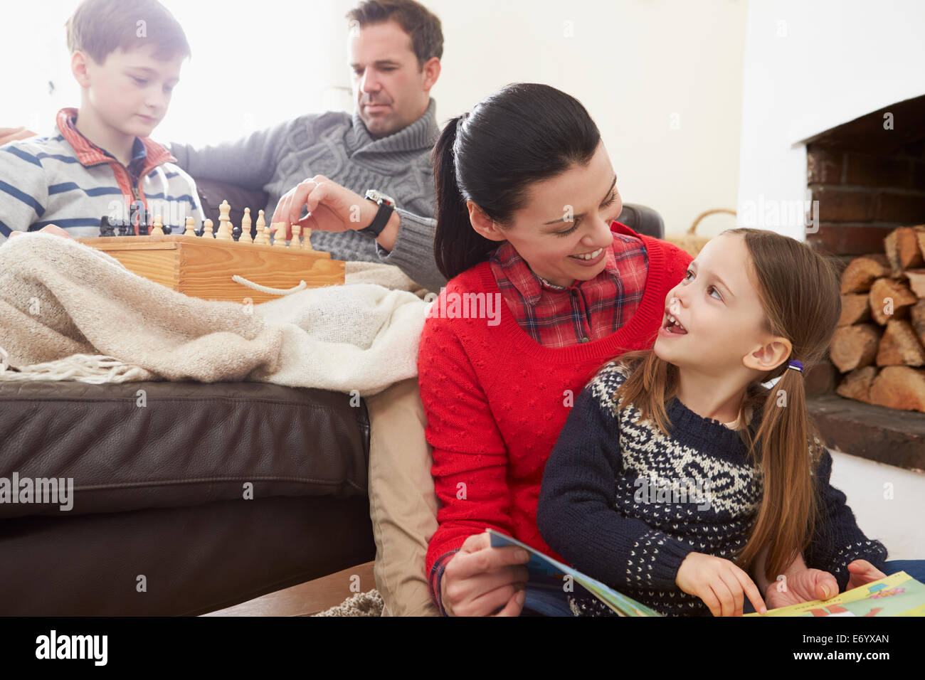 Family Relaxing Indoors Playing Chess And Reading Book Stock Photo